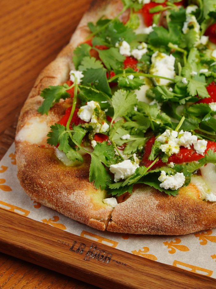 about-us Close-up of Italian pinsa topped with ricotta, cilantro, and greens.