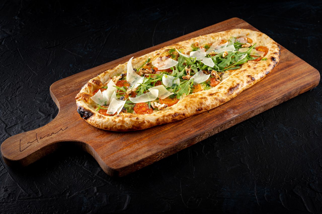 heros-img Savory flatbread topped with fresh arugula and parmesan on a rustic board.